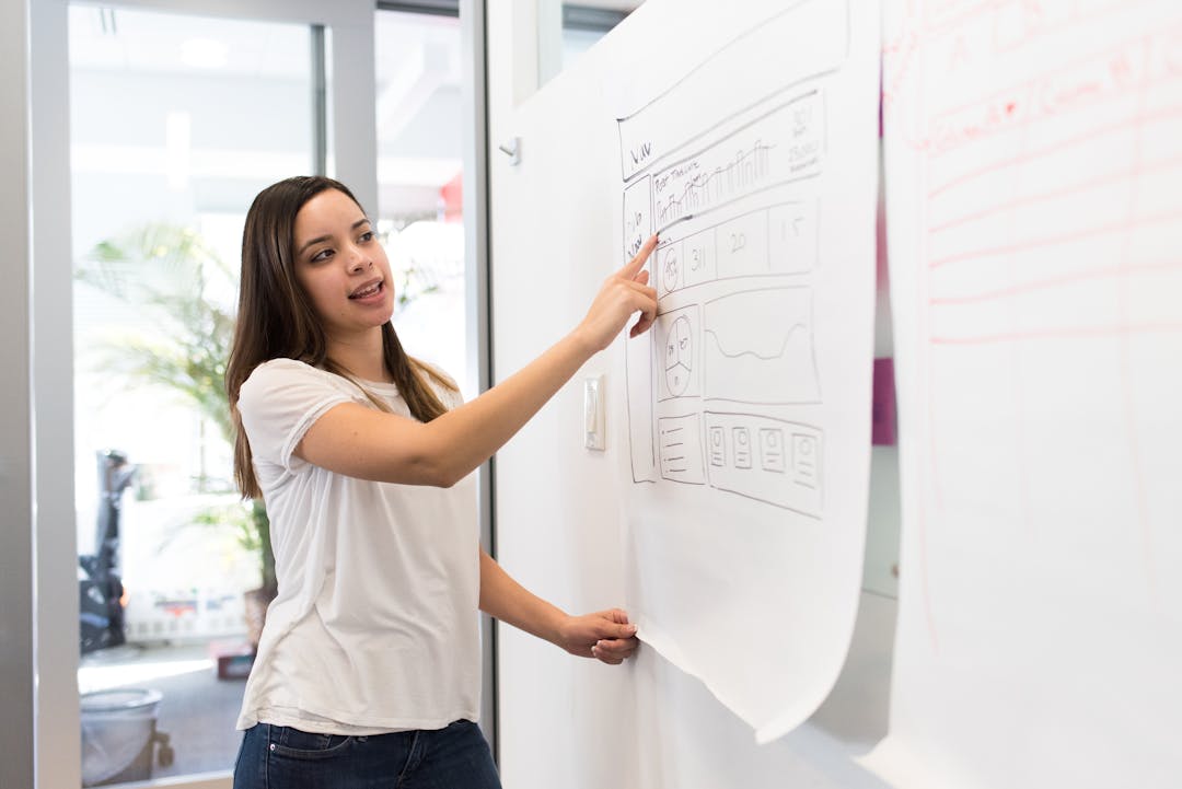Senior professional training younger employee at desk, pointing to documents and explaining processes