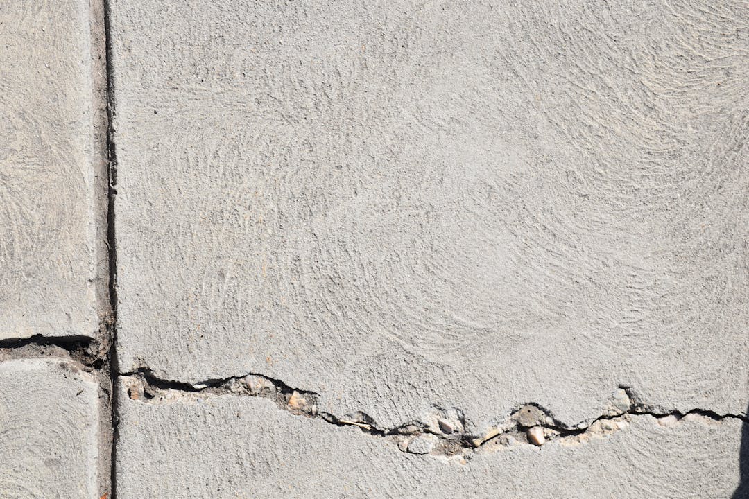 Close-up of cracked concrete foundation with repair tools showing structural vulnerabilities