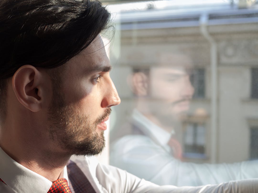 Person looking out window contemplatively during difficult decision-making moment