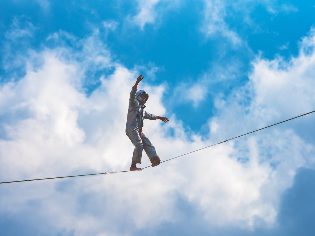 Silhouette of person carefully balancing on tightrope against cloudy sky