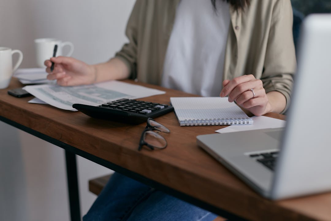 Person working with calculator and laptop on wooden table analyzing financial projections and scenarios