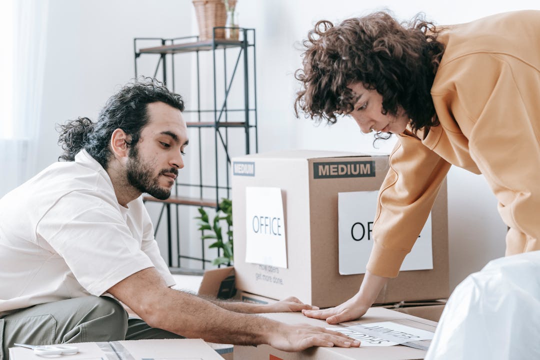 Cardboard moving boxes stacked in bright empty room with large windows