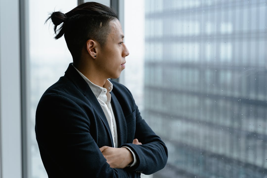 Thoughtful business owner sitting at desk reviewing documents, contemplative expression showing internal conflict
