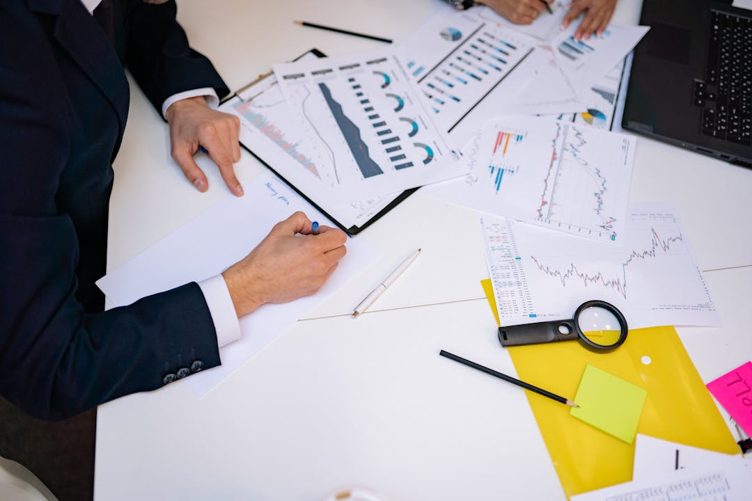 Magnifying glass examining detailed financial documents and spreadsheets on desk