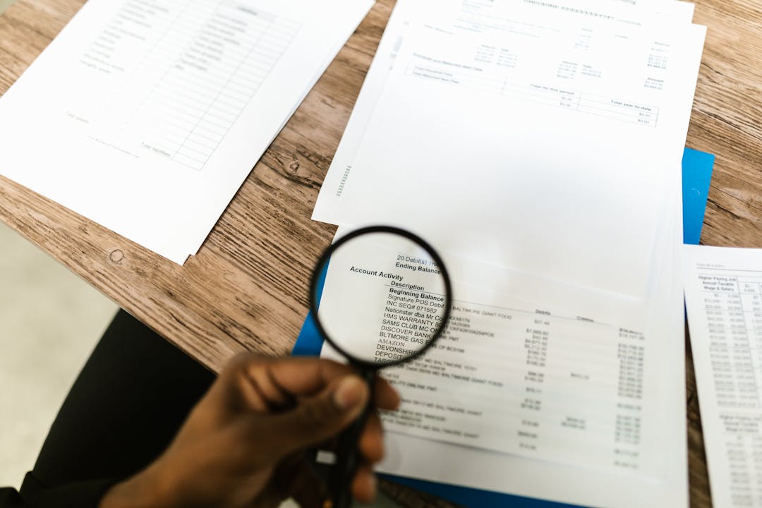 Professional using magnifying glass to examine detailed financial documents and charts