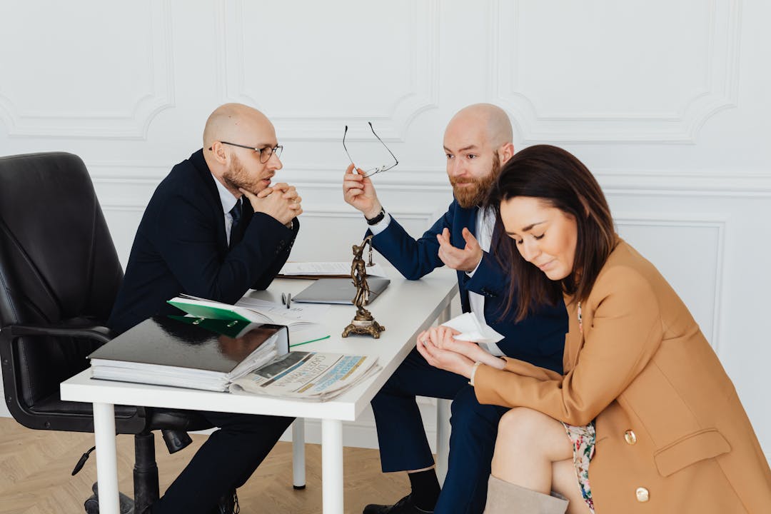 Two people reviewing documents across table with differing expressions, illustrating negotiation imbalance