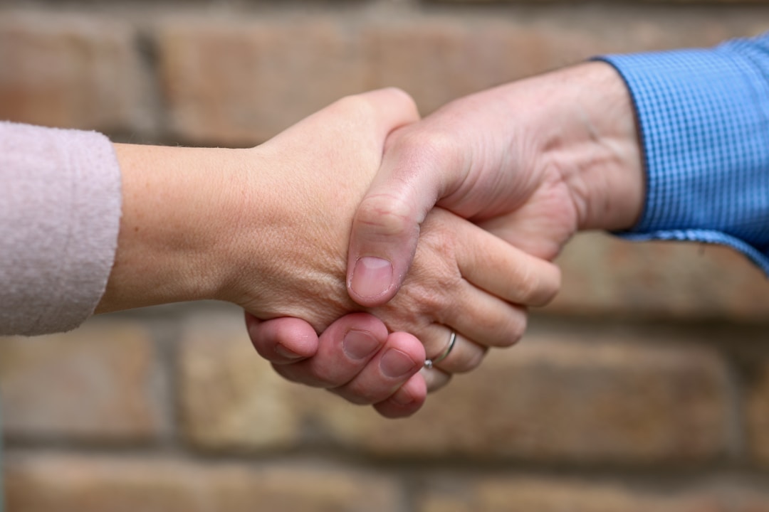 Two professionals shaking hands across negotiation table with contracts and documents