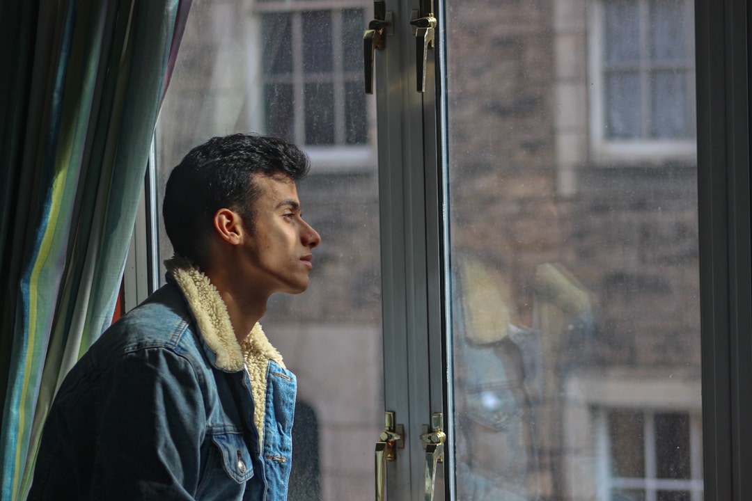 Person gazing out window with uncertain, reflective expression showing internal conflict